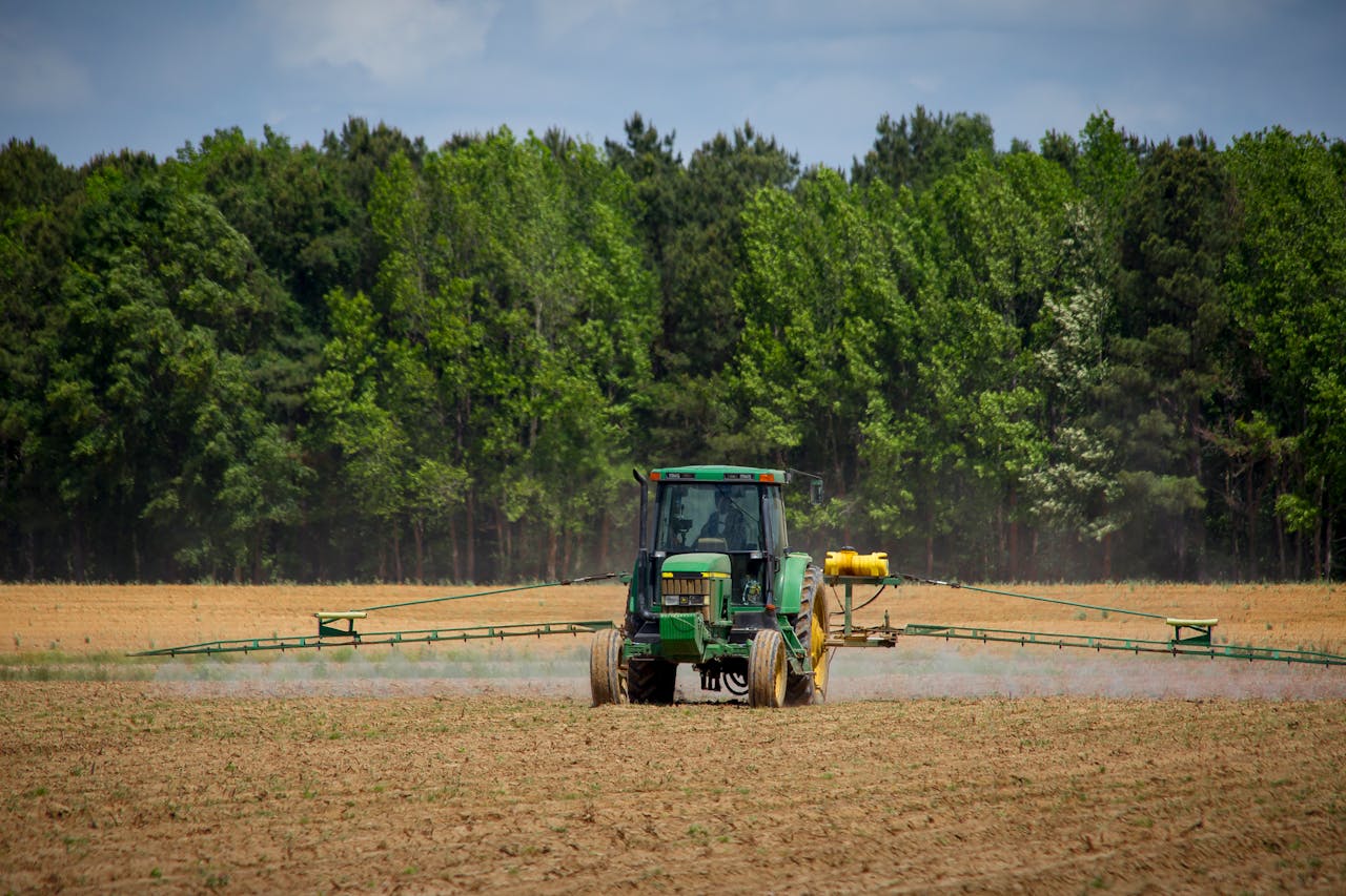 services-04 Tractor spraying fields with pesticides on a countryside farm in summer with a forest backdrop.